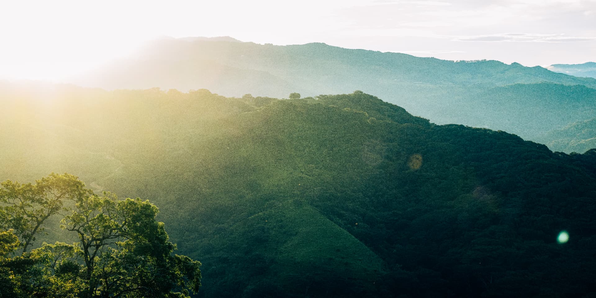 Sunlight spilling over layered green mountain ridges